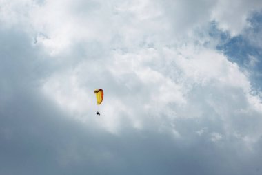 Sarı Paraglider tandem eğitmeni, güneşli bir günde bulutlarla gökyüzüne uçan bir turist..