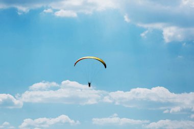 Sarı Paraglider, güneşli bir günde bulutlarla gökyüzüne uçuyor..