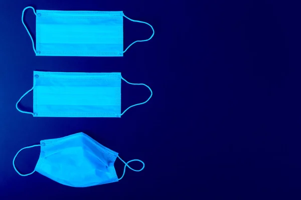 Three surgical medical masks used and unused are on an isolated blue background.