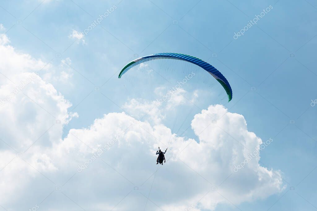 Blue Paraglider flying into the sky with clouds on a sunny day.