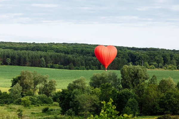 Red hot air balloon in shape of heart is landing on the green field — Stock Photo, Image