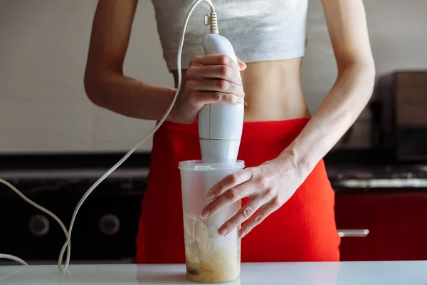 Woman with hand blender making sweet banana protein powder milkshake smoothie. protein shake after workout. sport nutrition diet after gym. Healthy lifestyle.