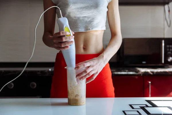 Woman with hand blender making sweet banana protein milkshake. sport nutrition diet after gym. Healthy lifestyle.