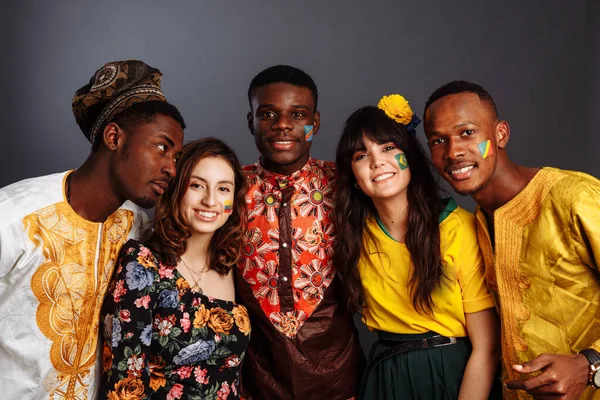 Peaceful Concept of friendship and peace between countries: three African men and two Latin ladies in national clothes smile and hug together with body arts flags Congo, Nigeria, Brazil, Ecuador