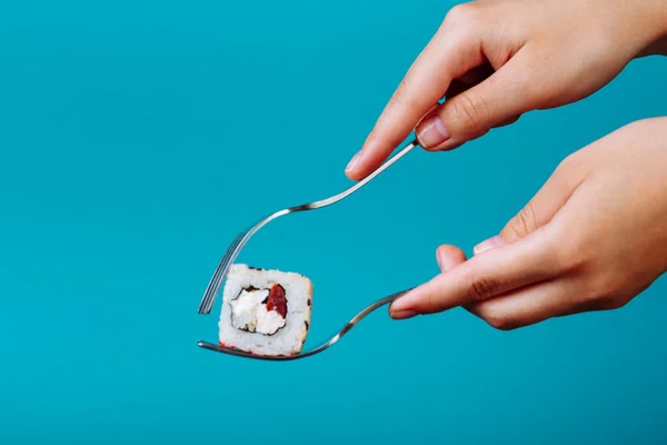 how to eat sushi roll with a fork, isolated on blue background. How to eat sushi without chopsticks.