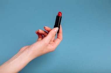 Kadının eli kırmızı ruj alıyor. Mavi arkaplanda izole edilmiş.