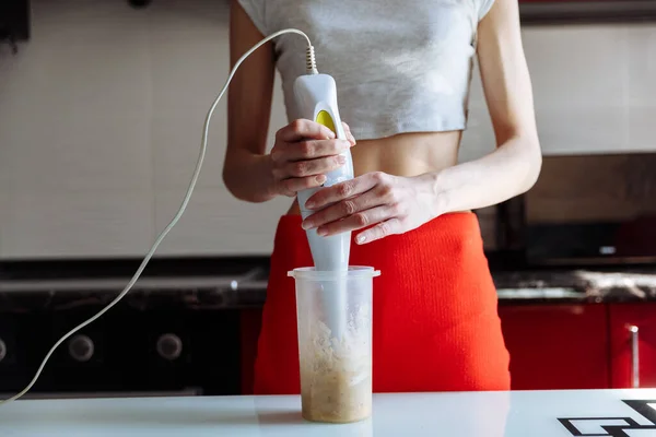 Woman with hand blender making sweet banana protein milkshake. sport nutrition diet after gym. Healthy lifestyle.