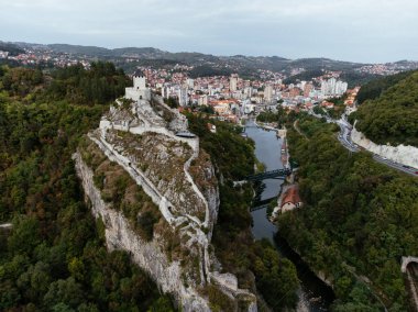 Sırbistan 'ın Uzice kentindeki nehre bakan ortaçağ uçurum tepesindeki kale ve kıvrımlı yolu olan kırmızı çatılı kasaba. g.