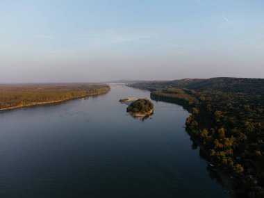 Gün batımında yemyeşil ormanlarla çevrili sakin bir nehir adasının havadan görüntüsü. g.