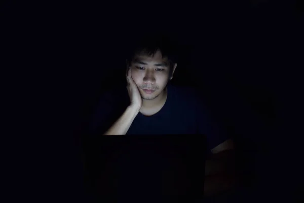 Asya adam siyah karanlık oda ve yüzünde bir şey düşünüyorum göstermek içinde laptop kullanma