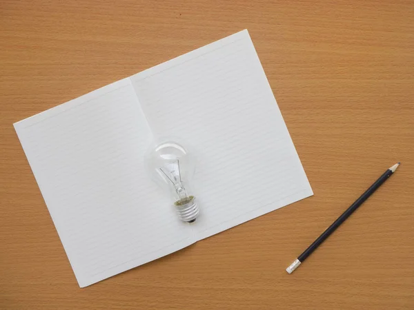 kopya alanı ile ahşap tabloda defter, ampul ve kalem üstten görünüm