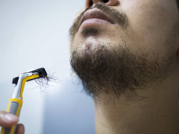 Closeup man use yellow shaver shaving messy beard and mustache on his face in bathroom — Stock Photo, Image