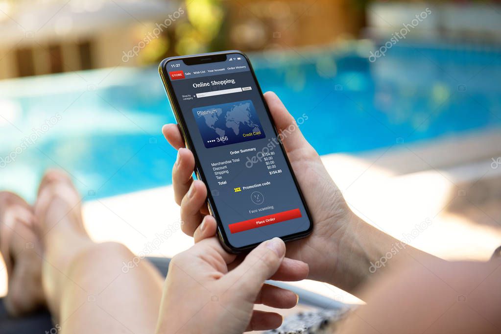 woman by the pool holding phone with app online shopping on the screen