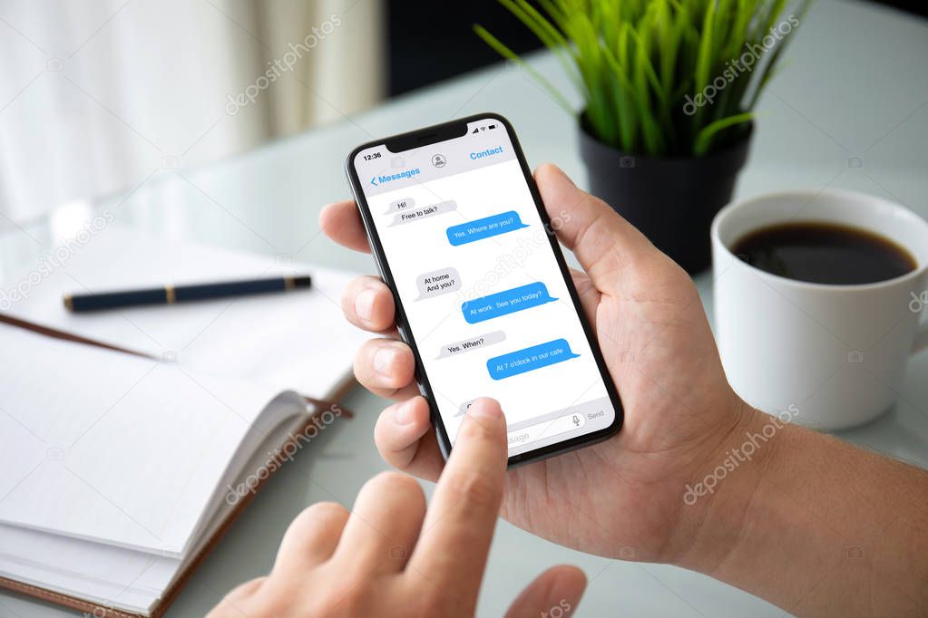 man hands holding phone with app messenger on the screen over table in the office 