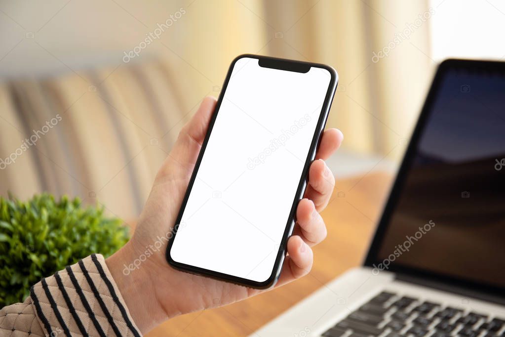female hand holding touch phone with isolated screen above the table with laptop in the office