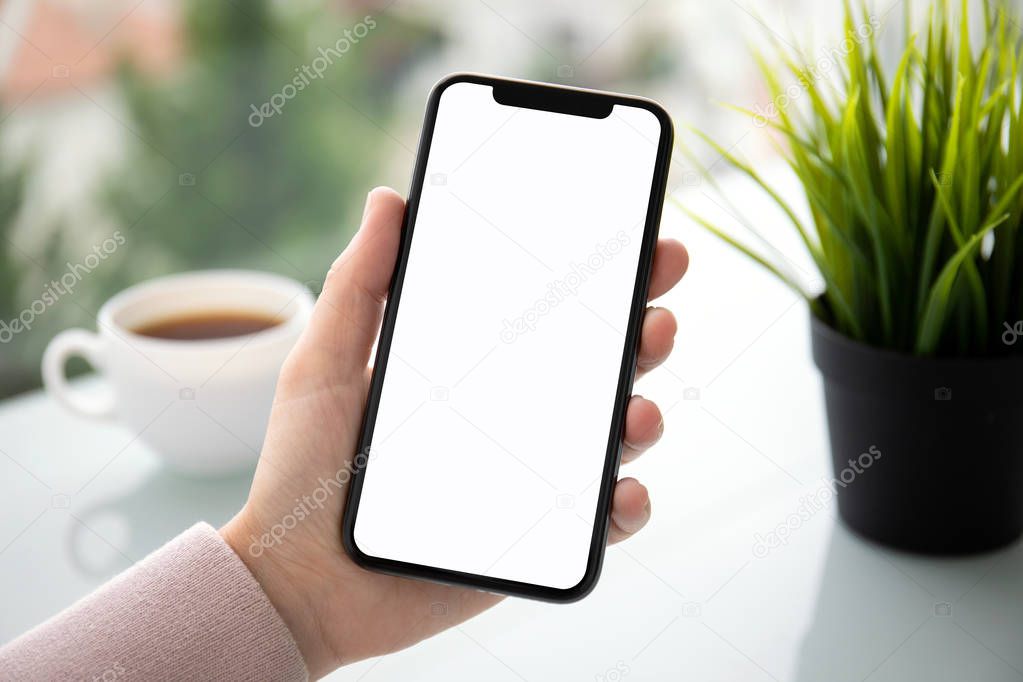 female hand holding touch phone with isolated screen above the table in cafe