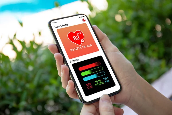 female hands holding phone with app heart and activity on screen and garden background