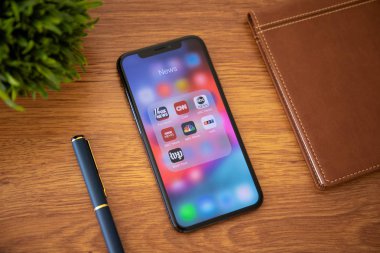 Alushta, Russia - October 13, 2018: iPhone X with popular news applications on the screen and background wooden desk. iPhone ten is created and developed by the Apple inc. clipart