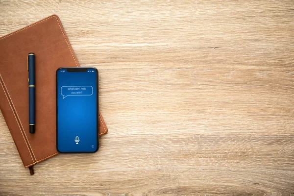 phone with app personal assistant on screen and wooden table with a notebook