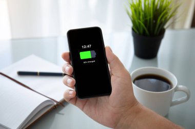 telefon şarj edilmiş bir batarya ile ekranda ofiste tabloda üzerinde tutan adam el