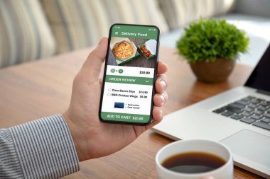 male hands holding phone with app delivery food on the screen above the table in the office