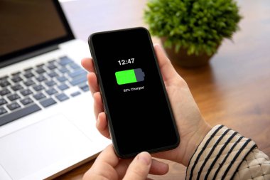 tablonun üst kısmındaki ofiste ekrandaki telefon şarj edilmiş bir batarya ile tutarak eller
