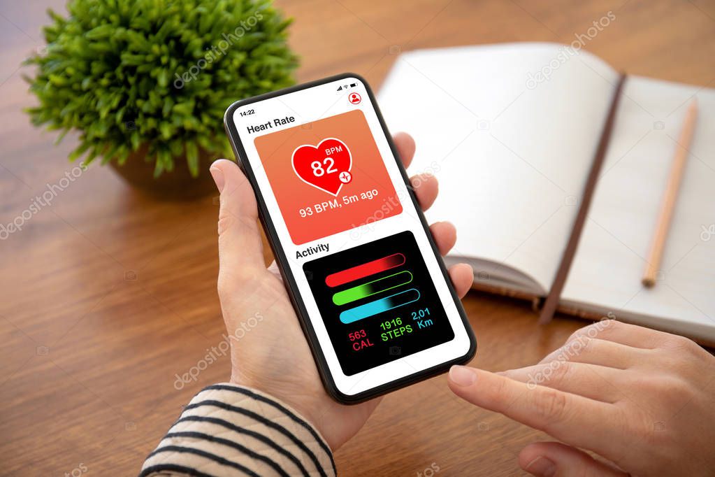 female hands holding phone with app heart and activity on the screen above table in office