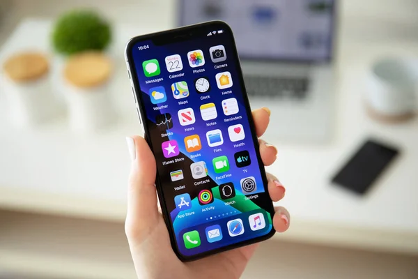 Woman hand holding iPhone X with home screen IOS 13 — Stock Photo, Image