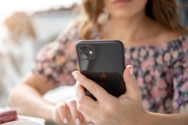 Apple iPhone 11 'i tutan ve masada oturan kadın.