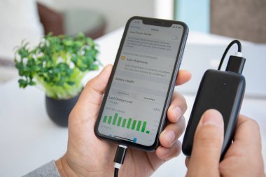 Alanya, Türkiye - 28 Mayıs 2020: Powerbank RavPower ve iPhone 11 ile el ele tutuşan adam ekranda Pil uygulaması.
