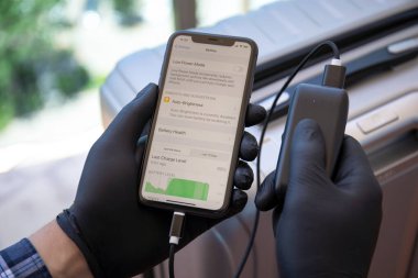 Alanya, Türkiye - 23 Mayıs 2020: Siyah eldivenli adam elinde iPhone 11 ve ekranda uygulama pili ve bagajda Powerbank RavPower.