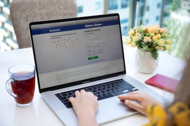 Alanya, Türkiye - 6 Haziran 2020: Ekran laptopunda sosyal ağ hizmeti Facebook 'u olan Macbook Pro 16' yı masaya yatıran kadın.