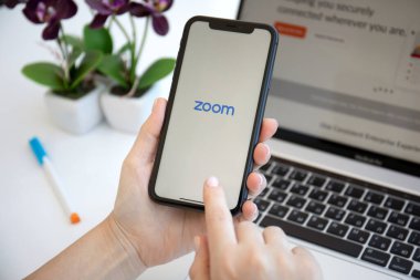 Alanya, Türkiye - 6 Haziran 2020: Kadın eli iPhone 11 ve Macbook Pro 16 ekranda Zoom Video İletişim uygulamasını arıyor.