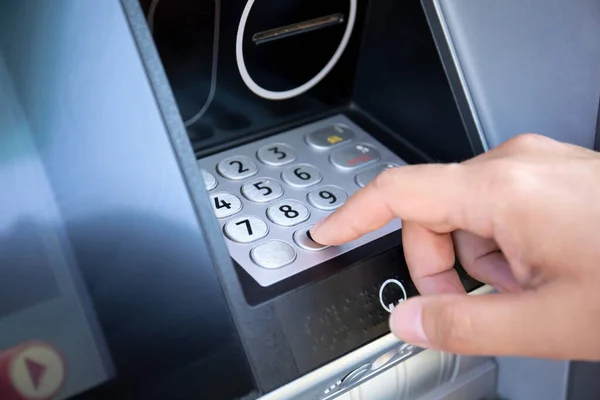 male hand dials the pin code on the buttons of the ATM