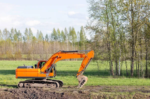 Orange excavator on the background of a meadow and trees