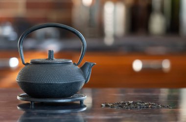 Siyah metal çaydanlık ve çay yaprakları masada.