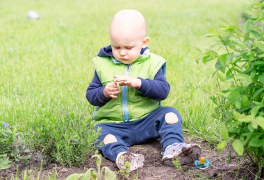 Kirli elleri olan bir çocuk, taze yeşilliğin arka planına karşı yerde oturur.