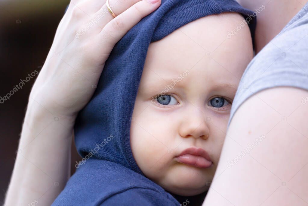 A sad little boy with a hood on his head snuggles up to his mother
