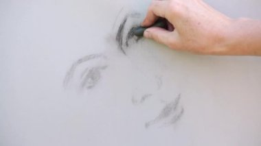 Pastel boya kaleminde bir kadının yüzünü çizen bir el.