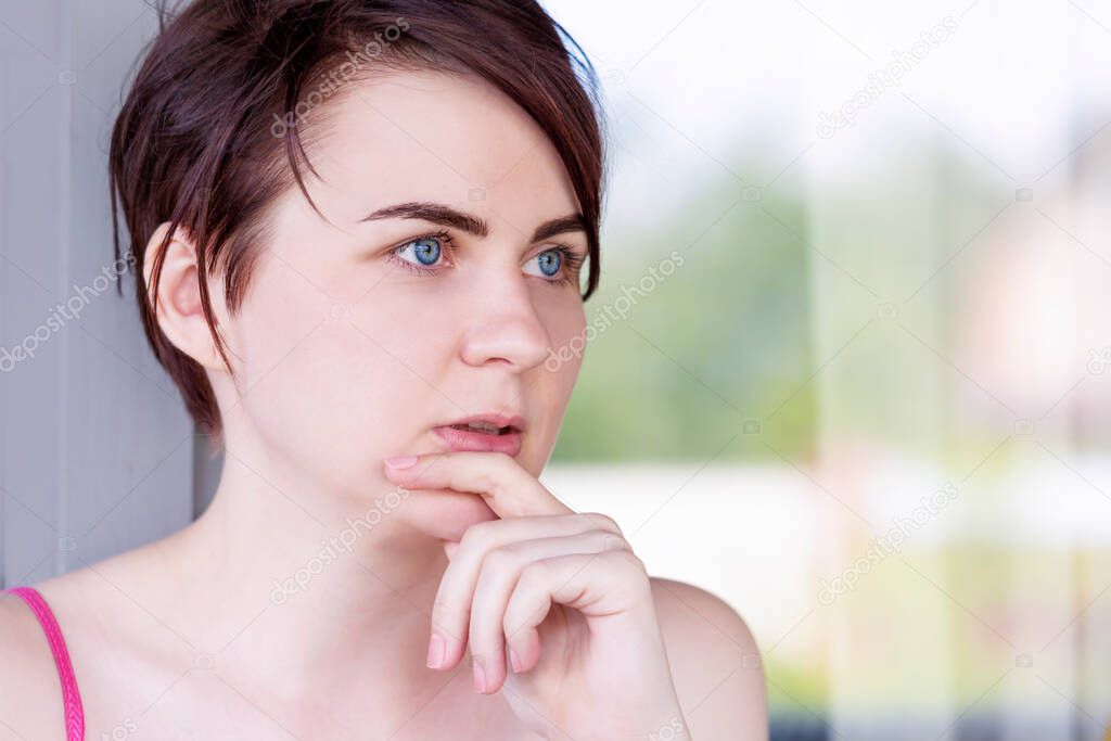 A blue-eyed brunette with short hair and wide dark eyebrows puts a finger to her chin thoughtfully