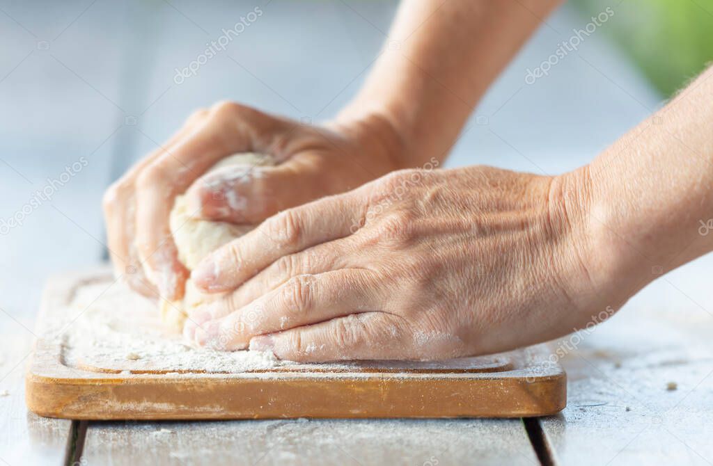 Close-up of women's hands kneading dough on a cutting board in the early morning