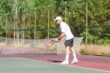 Fiziksel olarak iyi durumda yaşlı bir adam güneşli bir günde dışarıda tenis oynar.