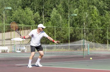 Fiziksel olarak iyi durumda yaşlı bir adam güneşli bir günde dışarıda tenis oynar.