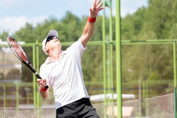 An elderly tennis player in good physical shape plays tennis on an outdoor court on a sunny day