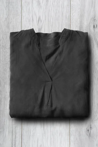 Folded black silk blouse on white wooden background