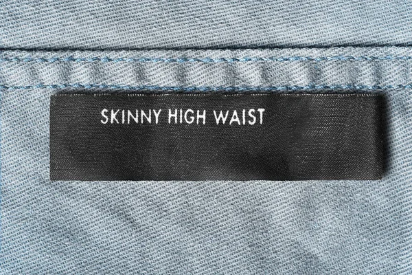 Clothes label says skinny high waist on blue denim background