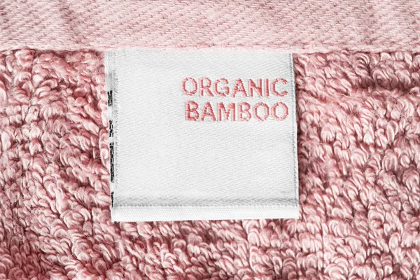 Clothes label says organic bamboo on pink textile background closeup