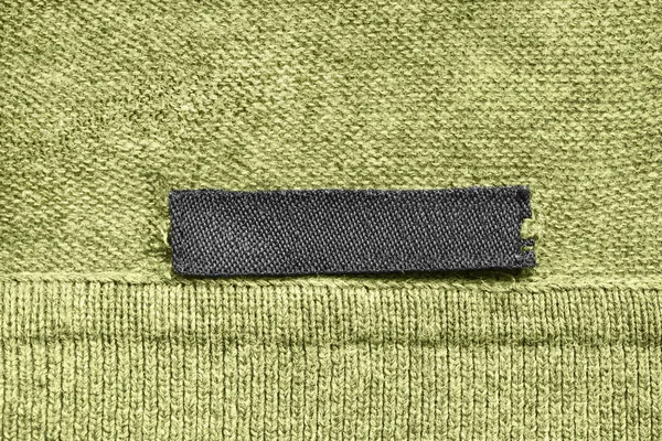 Textil Schwarzer Leerer Kleidungsaufkleber Auf Grünem Strickhintergrund — Stockfoto