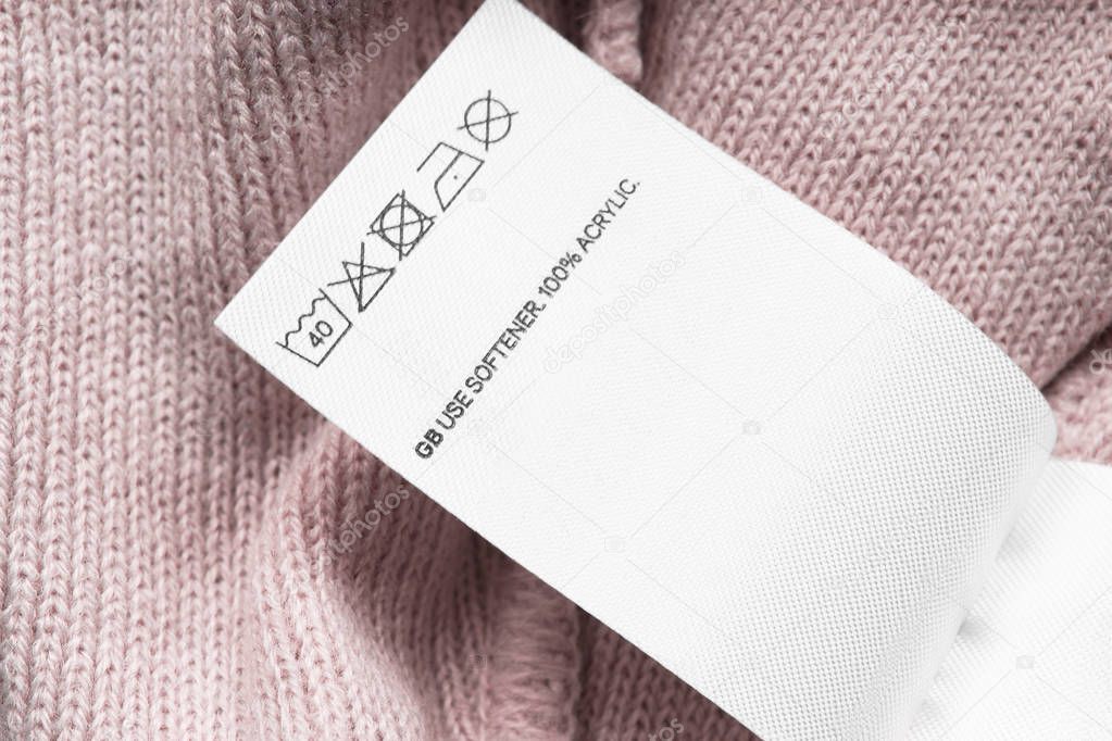 Care and composition clothes label on pink knitted background closeup