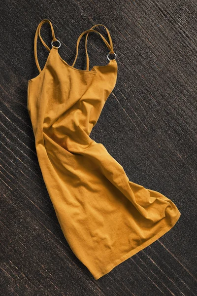 Yellow crumpled cotton dress on dark brown wooden background